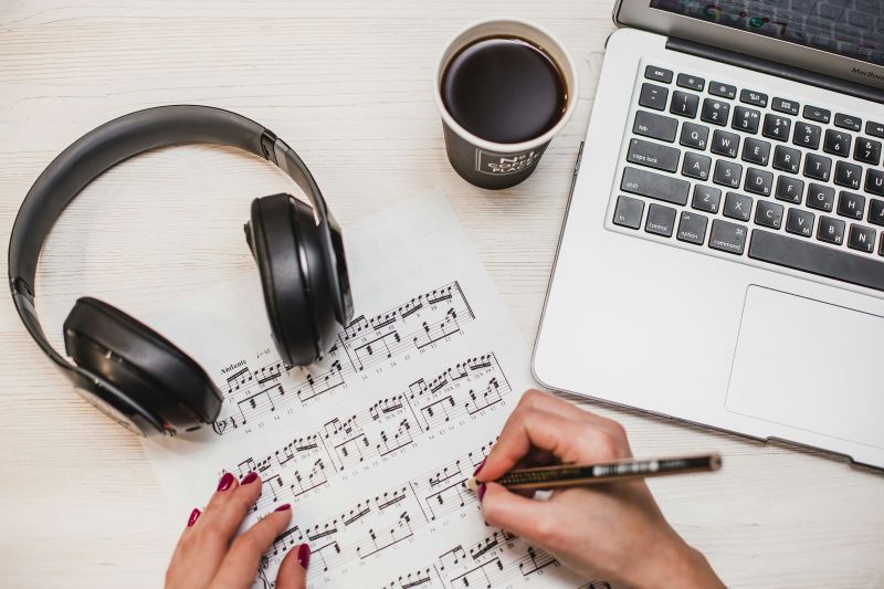 Mac, headset og to hender som noterer på et noteark